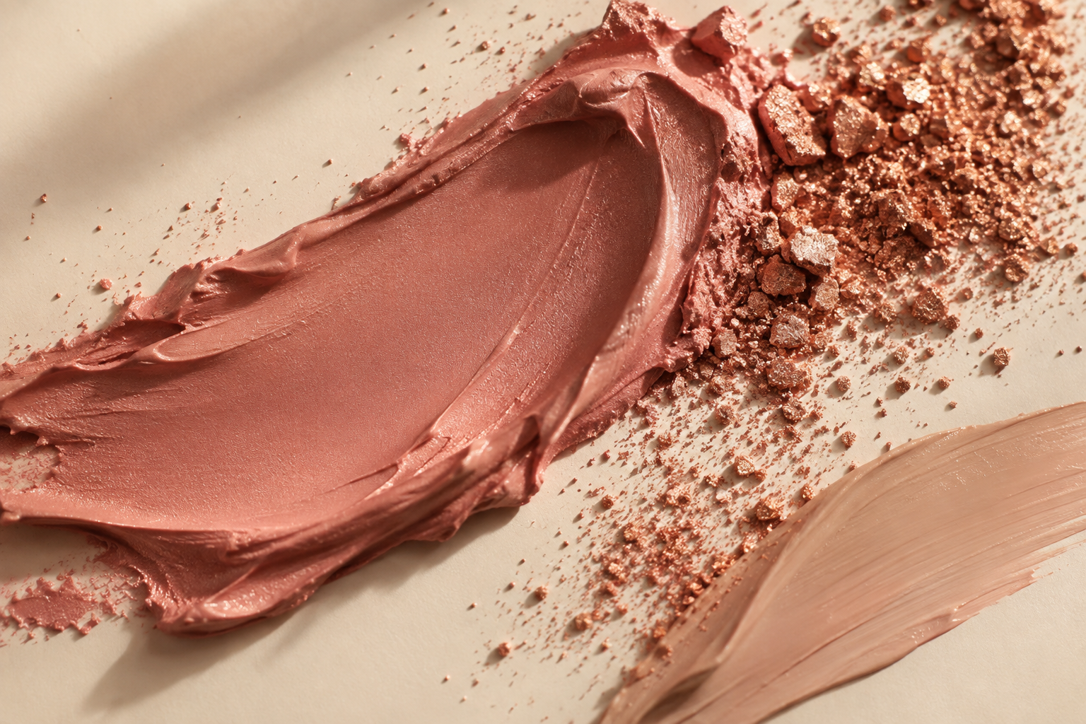 Texturas de maquillaje en crema y pigmentos rosa y cobre sobre fondo marfil